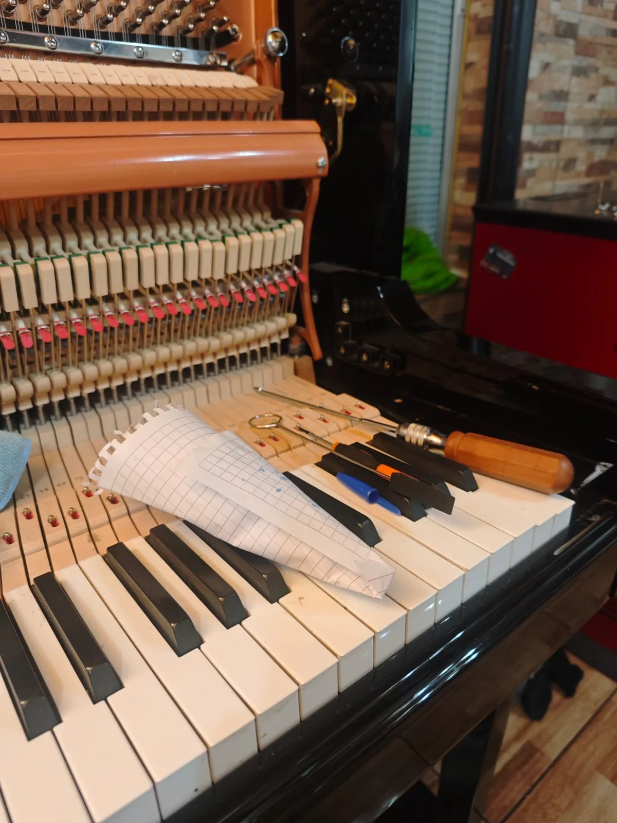 Herramientas de afinación profesional | tecnicopiano.cl Llave de afinación y cuñas sobre teclado de piano vertical con mecanismo expuesto — tecnicopiano.cl